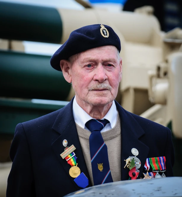 older man in blue uniform standing beside large artillery equipment