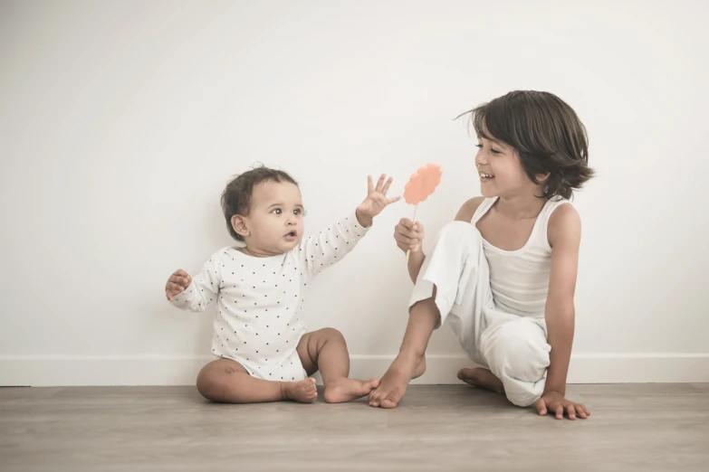 two babies are sitting on the floor and smiling