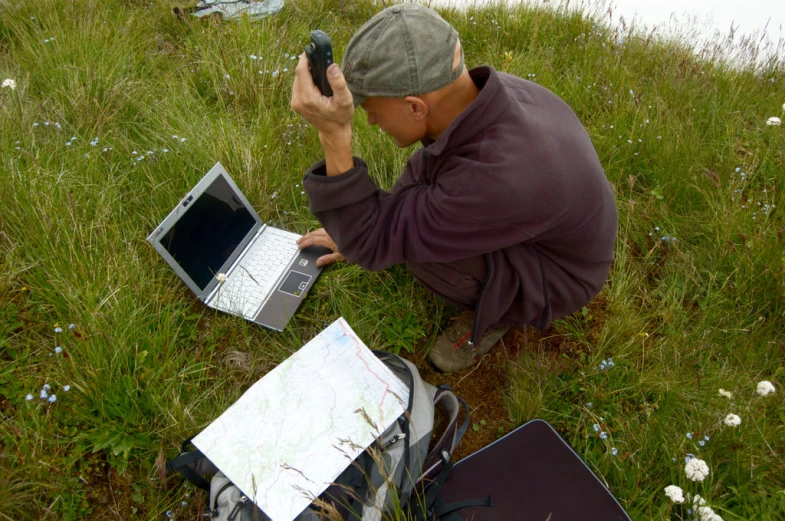 a man is sitting in a field working on his laptop