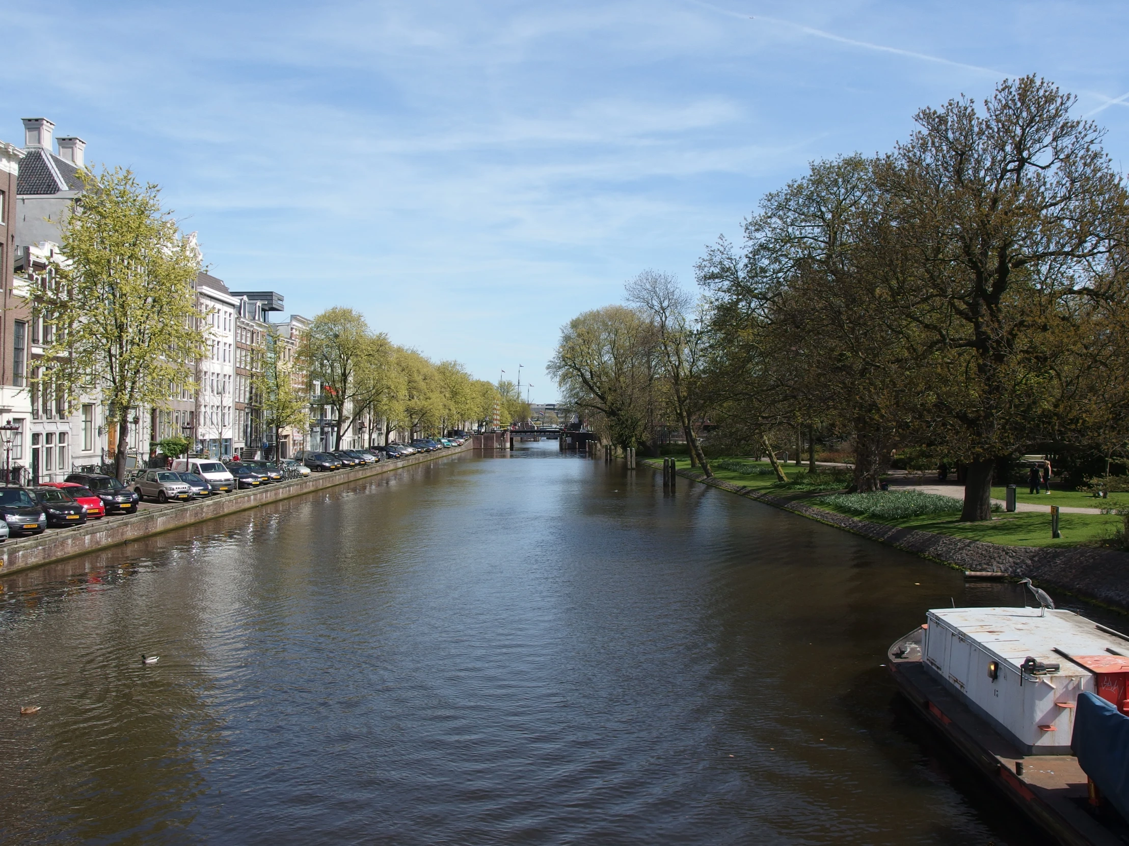 an empty canal with buildings, parked cars, and several trees