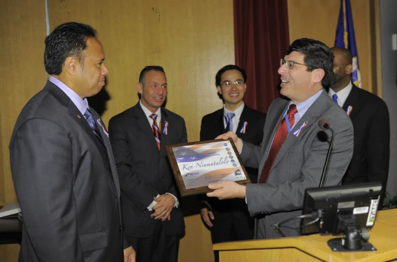 man presents award to colleague on stage with other men