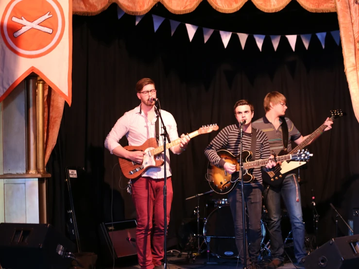 three men in an auditorium singing with guitars