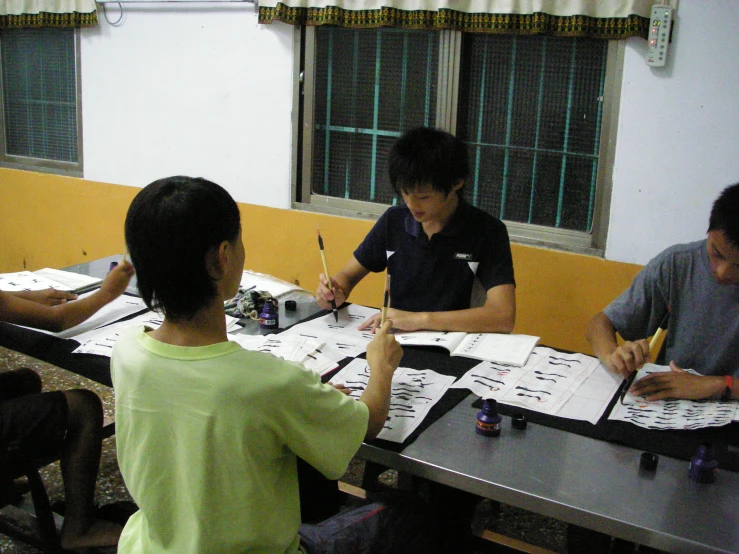 three people are sitting at a table doing work on papers