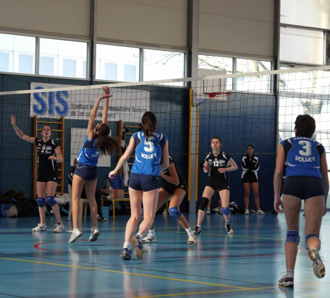 girls in uniforms playing volleyball on a indoor court