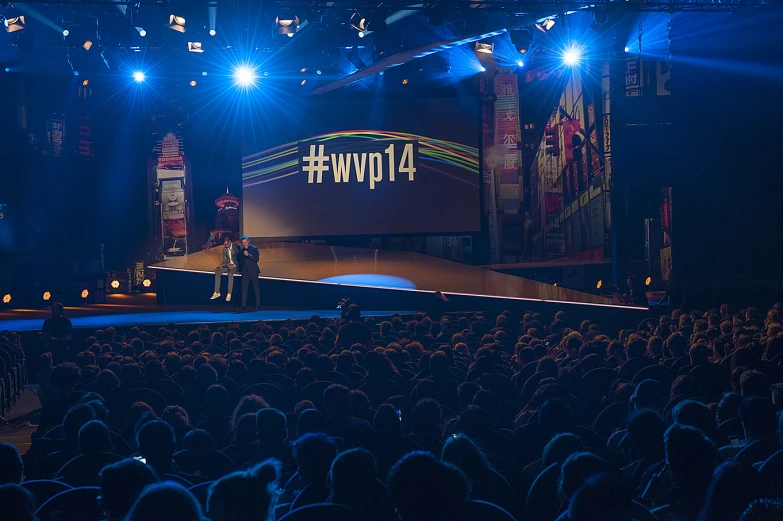 an event in a convention hall with people at podiums and on stage, illuminated by bright lighting