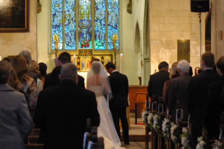 a bride and groom stand at the alter as other people look on