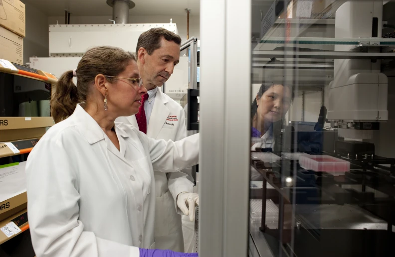 two people in lab coats standing by a shelf