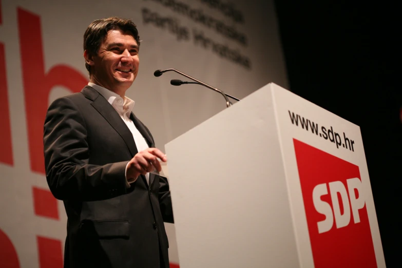 a man speaking on stage with a sign in front of him