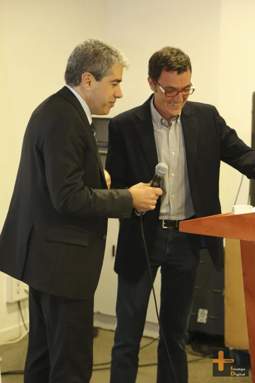 two men stand at a podium while a microphone is hooked up to one another