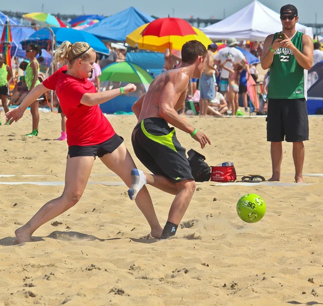 two people playing a game of beach soccer on the sand