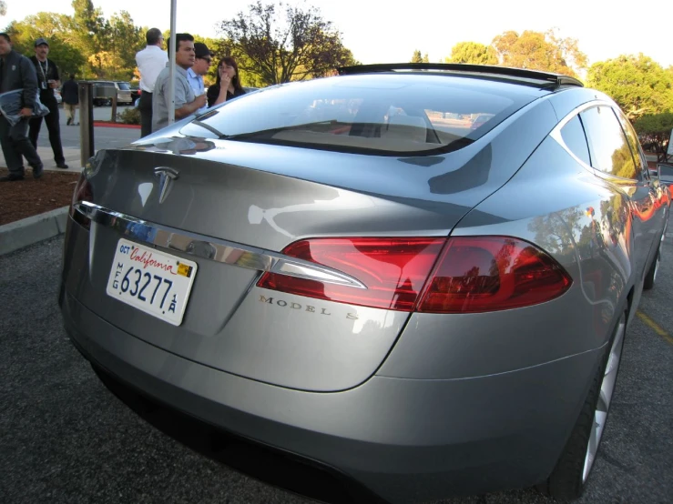 a silver car parked on a street next to people