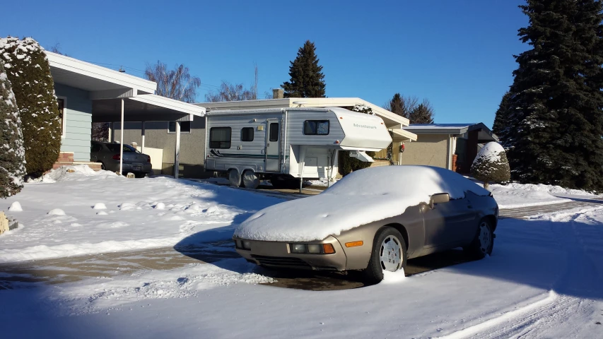 a car covered in snow sits on a residential street near homes