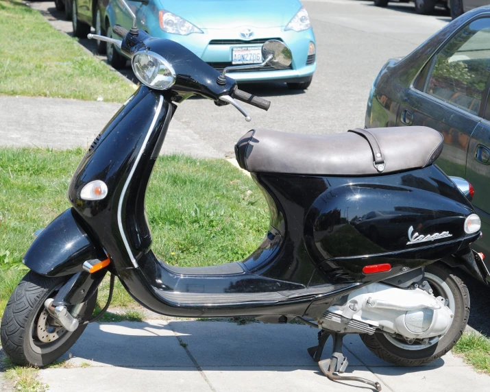 this moped is parked next to the sidewalk near some parked cars