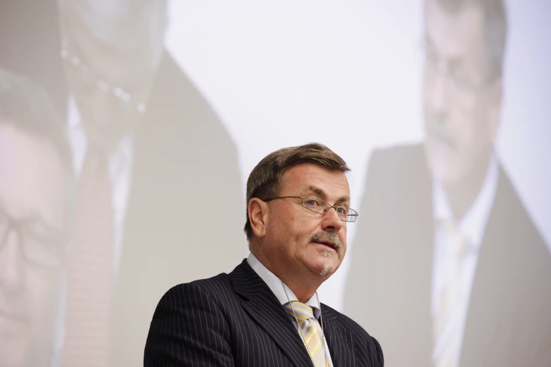 a man in suit and tie standing in front of a projector screen