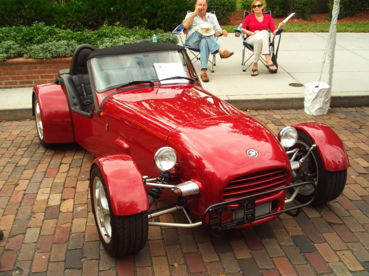 two people sitting down talking near a classic car