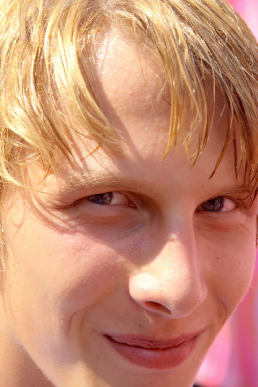 young blonde man with messy hair smiles while holding a phone