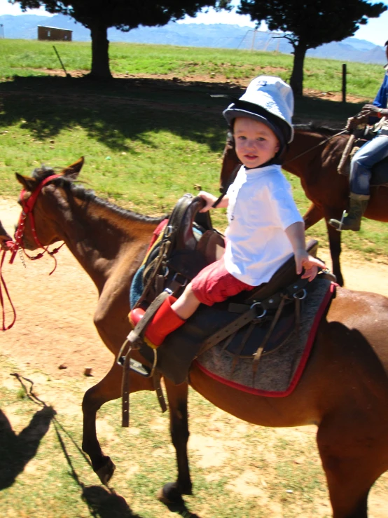 a small boy riding a horse with another little girl