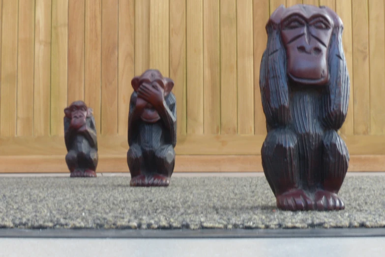 three ceramic monkeys in front of a wooden fence