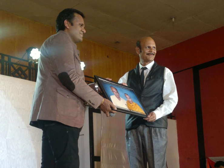 two men are standing at the podium holding a framed pograph