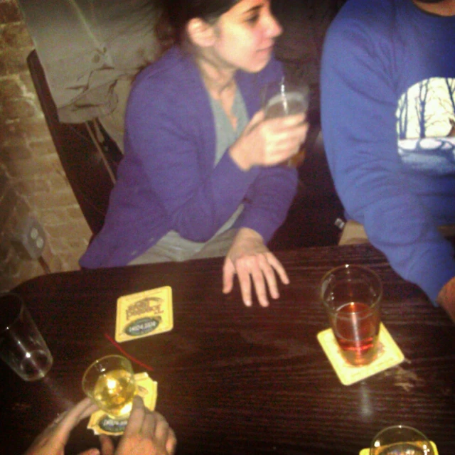 a woman sits at a table holding up wine glasses