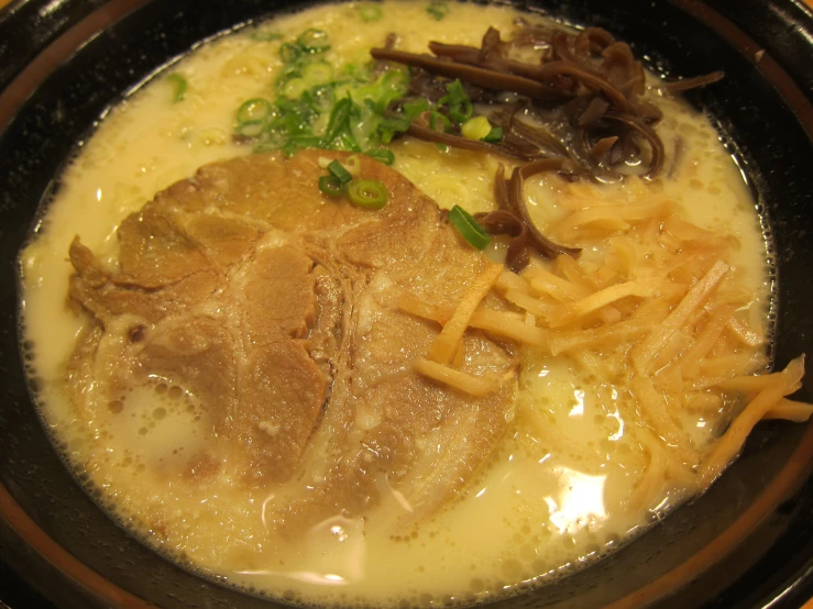 a black bowl containing noodles, meat and other ingredients