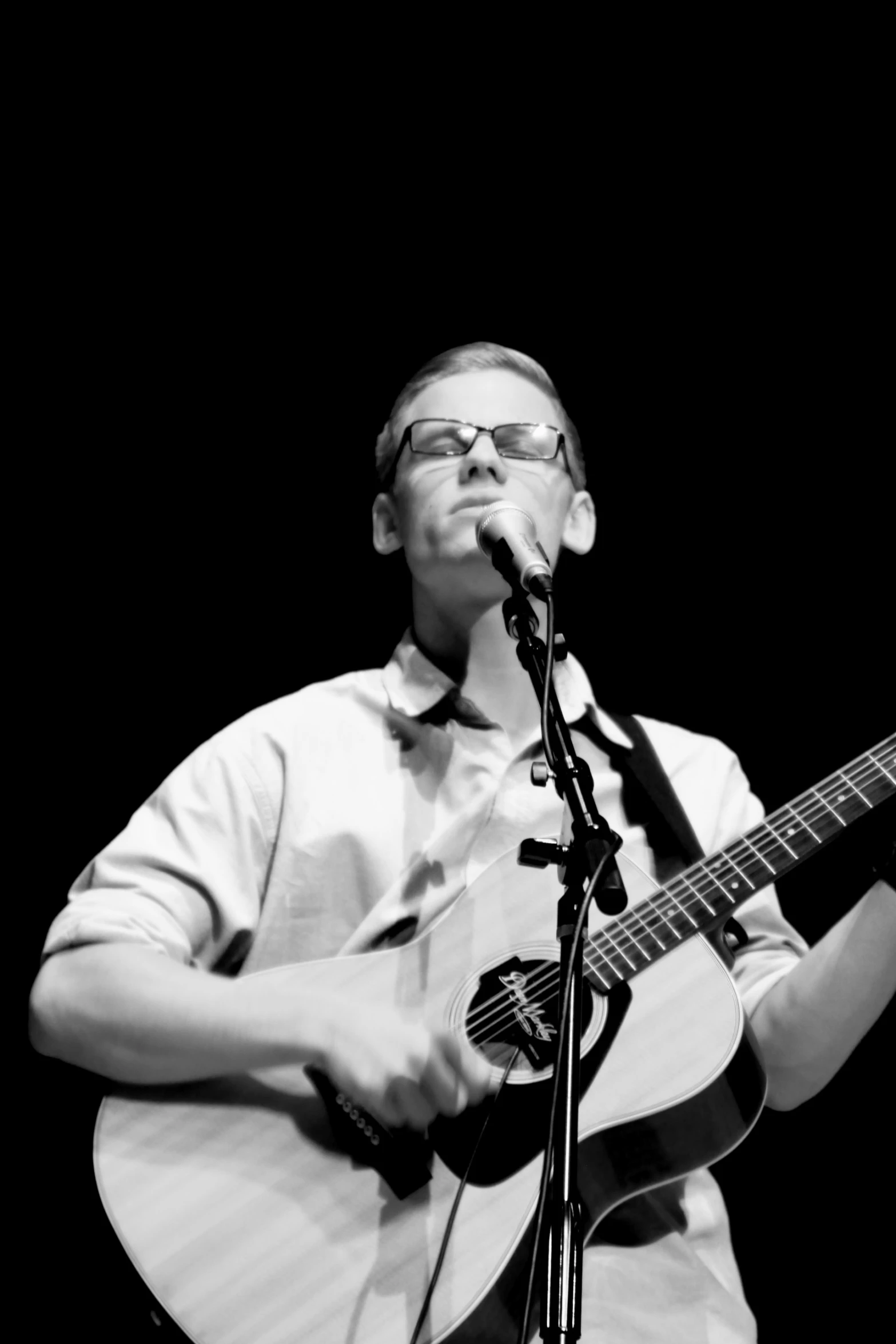 a man in glasses playing a guitar while singing into a microphone
