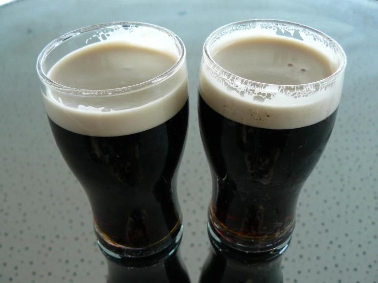 two dark beers sitting on top of a glass table