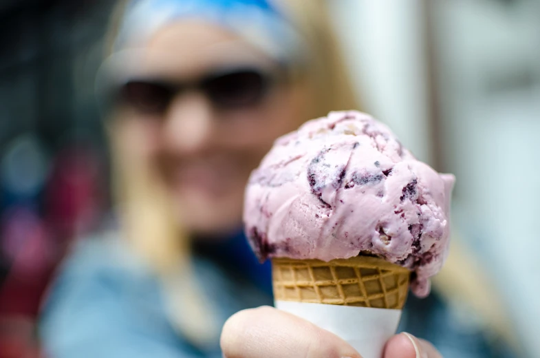 a hand holding an ice cream cone with a pink topping on it