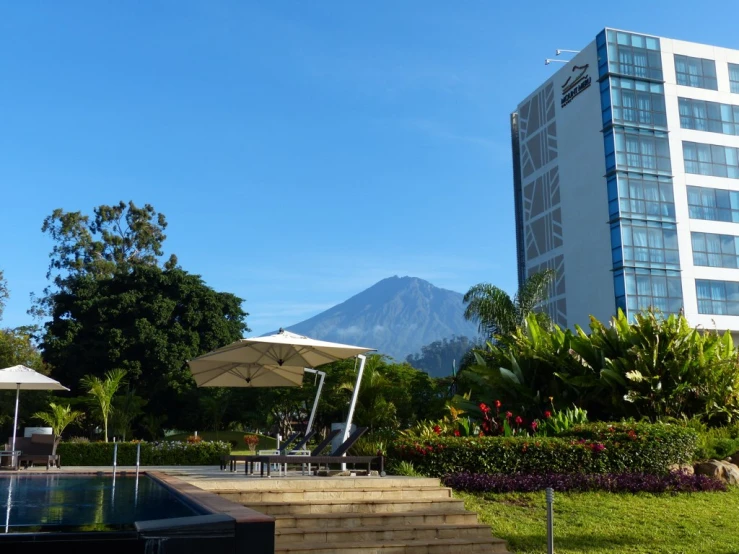 an outdoor pool area near several umbrellas and a building with a mountain behind