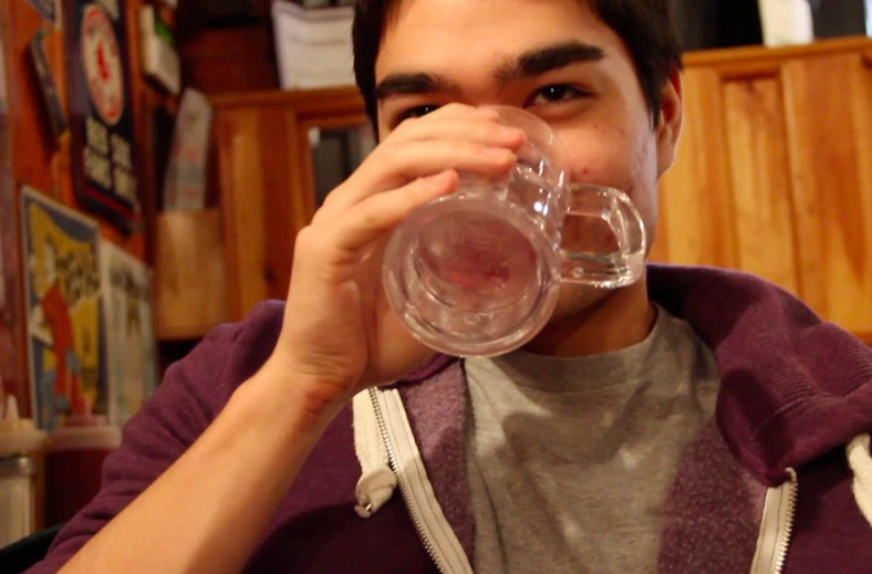 man in grey shirt drinking from a clear glass