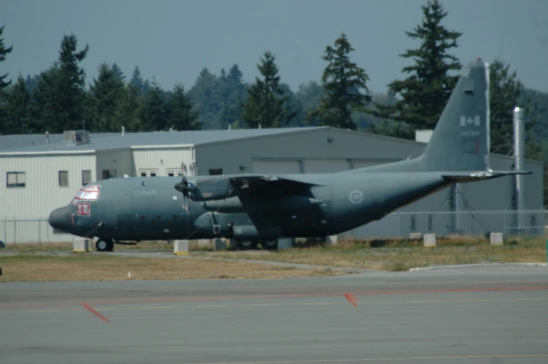 a large gray plane on runway next to buildings