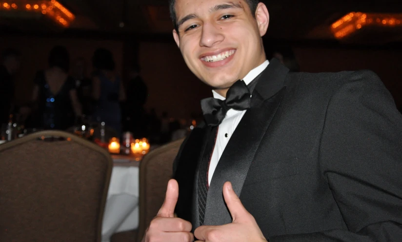 a young man in a tuxedo giving a thumbs up