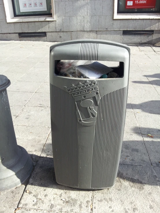 a trash can is on a sidewalk near a pole