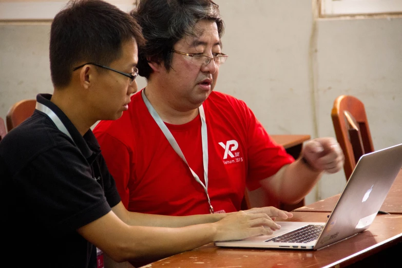 two men sitting at a table with a laptop computer