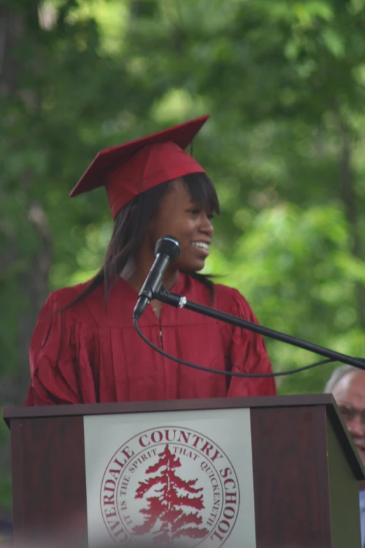 a woman in a red graduation gown stands at a podium