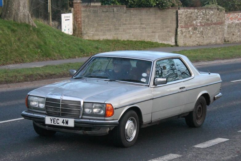 a silver car on road next to wall and grass