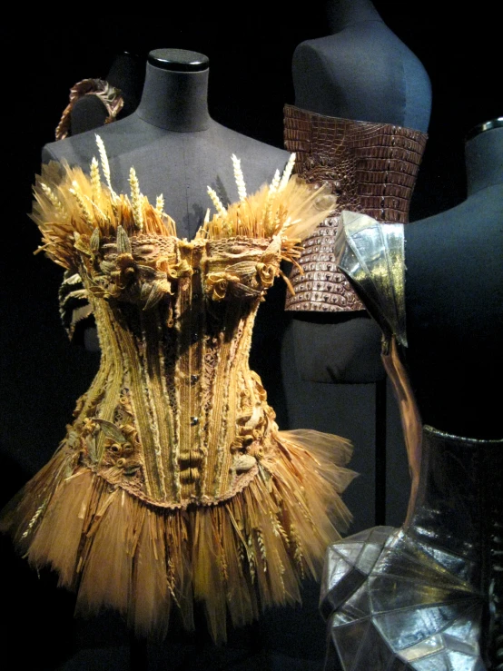 three black mannequins with yellow tulle, each one has gold feathers on it