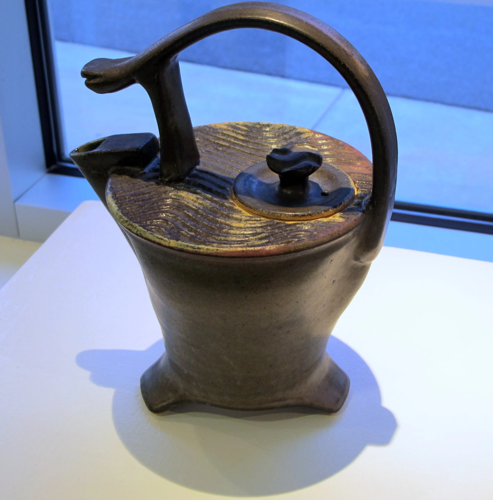 a pottery vase with handle sitting next to a window