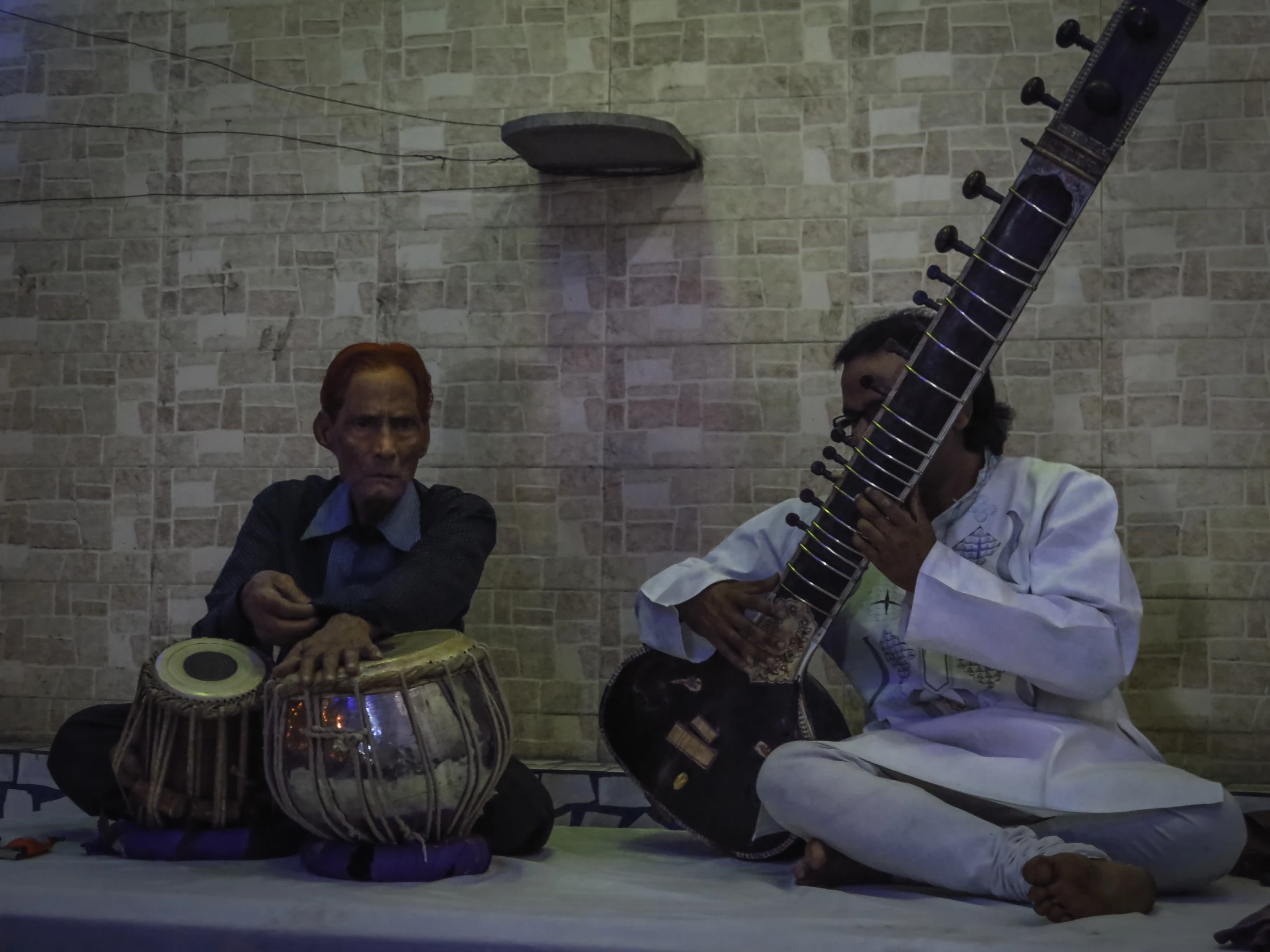 an indian man plays a sit down musical instrument next to a woman