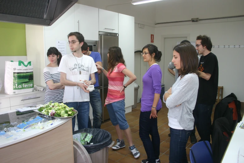 there are people standing in the kitchen with items in the background