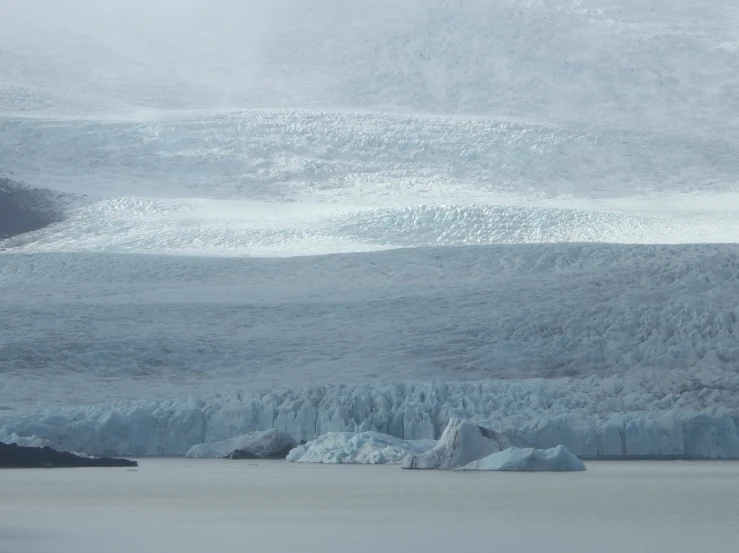 a iceberg with water coming from it and snow covered mountain in the background