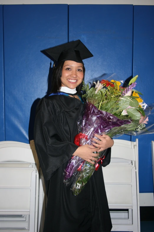 a smiling female graduate holding flowers and wearing a cap