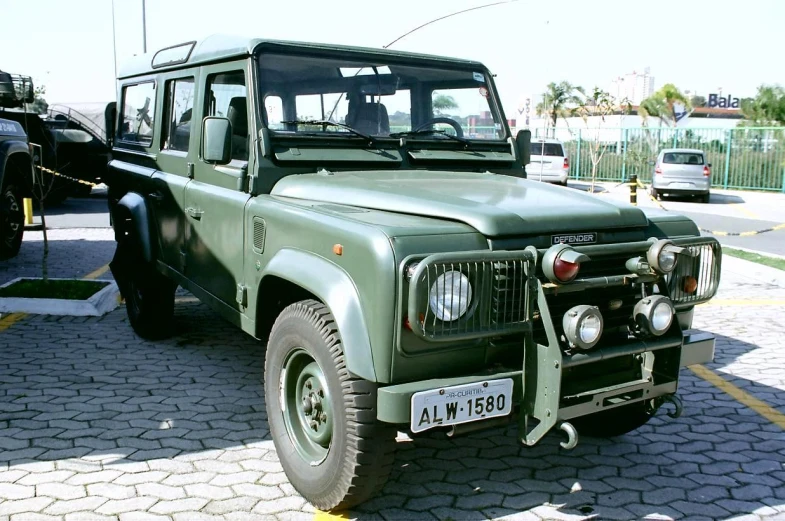 green land rover vehicle parked on pavement next to two parked cars