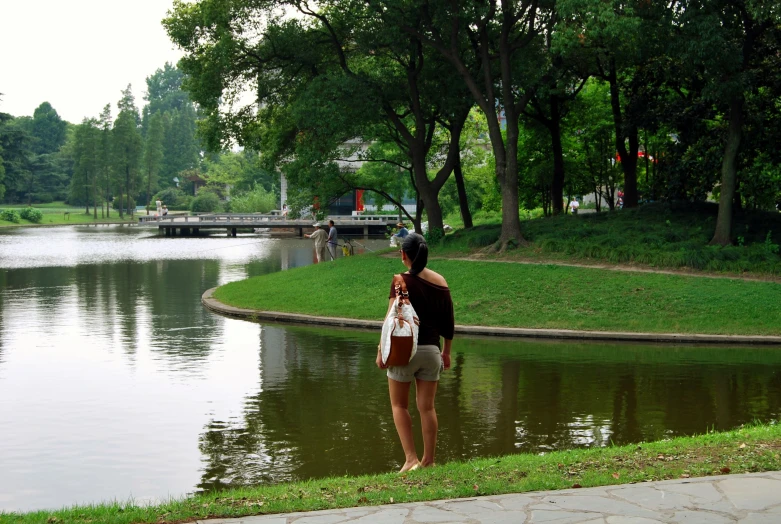 a woman standing on the grass next to a pond