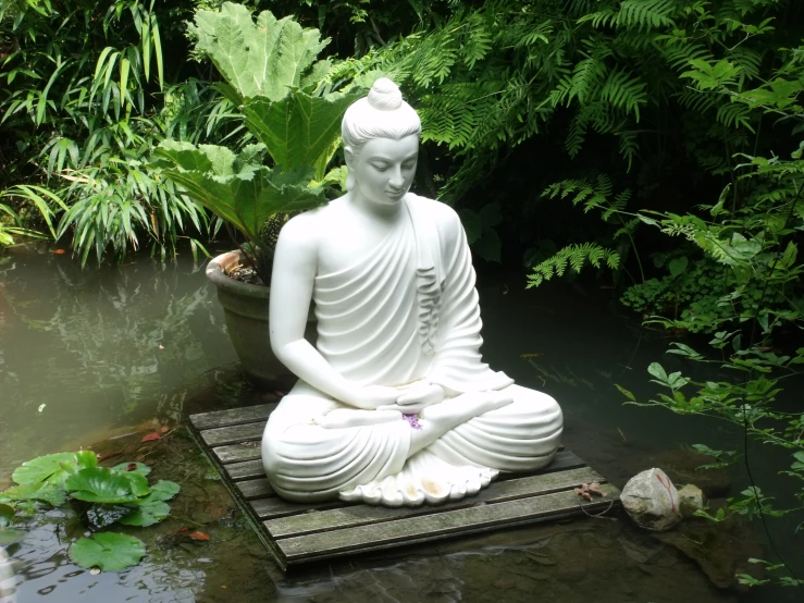 a buddha statue sitting on top of a stepping platform near a small pond