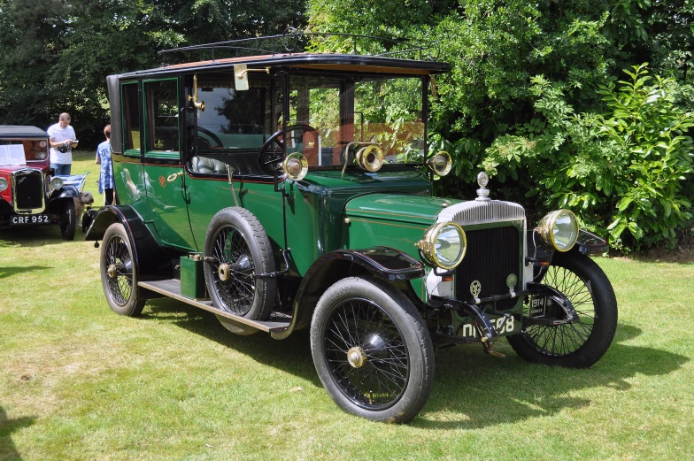 an old green car sits parked on grass