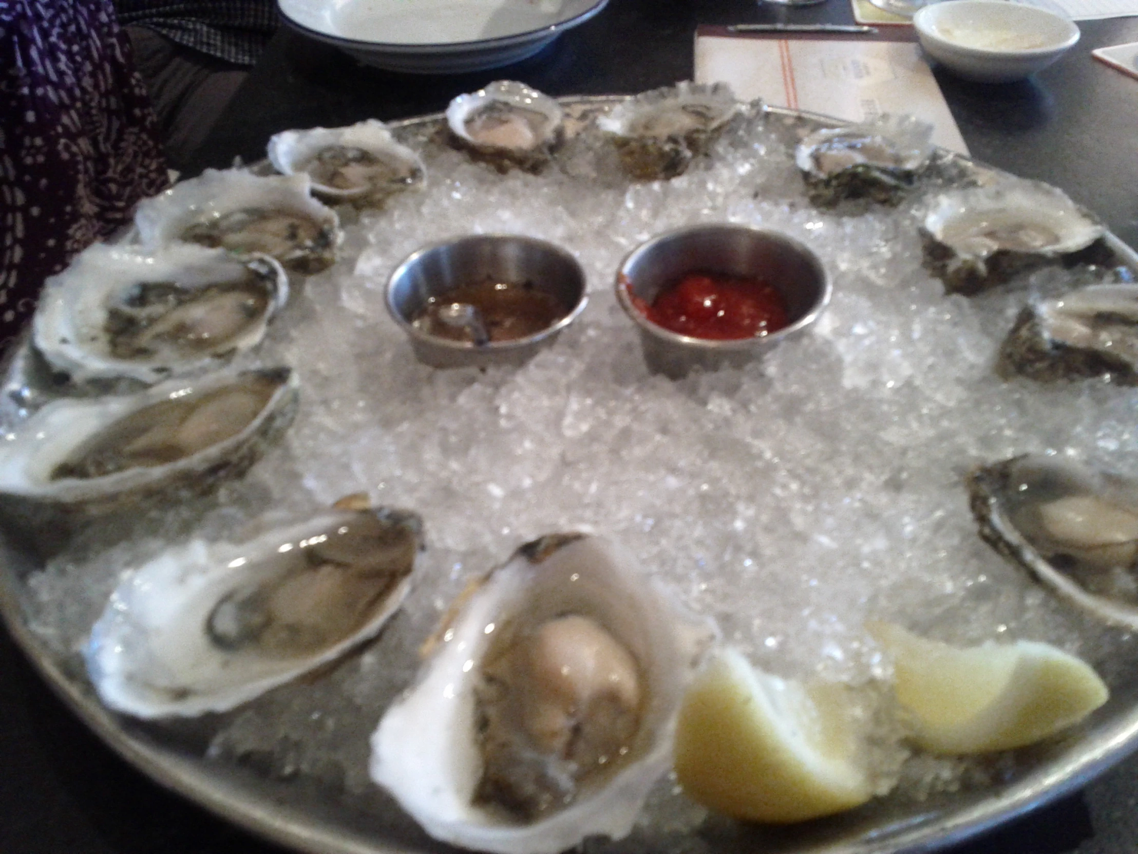 a platter of fresh oysters on ice, served with dipping sauce