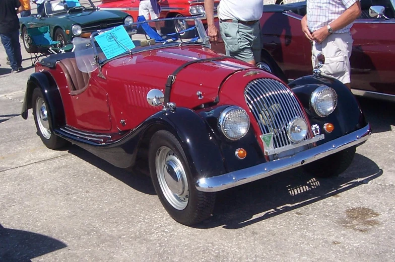 an old vintage buggy with a flat head and three wheels parked next to other vintage cars