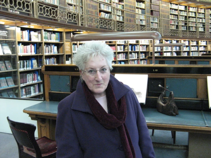 a lady posing in front of a bookshelf with chairs