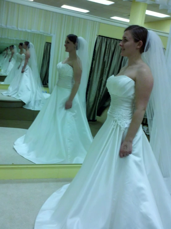 two women wearing wedding gowns in front of a mirror